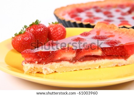 Piece of Strawberry Tart on a yellow plate decorated with strawberries with a tart in a tart pan in the background