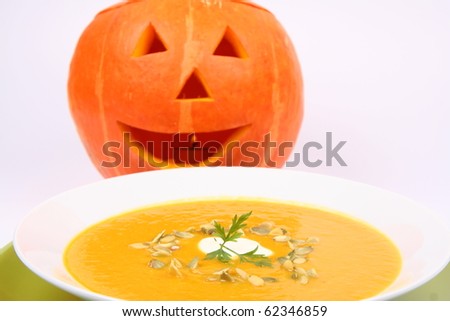 Pumpkin soup decorated with cream, pumpkin seeds and parsley with Jack-o\'-lantern in the background