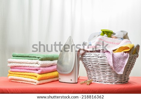 White iron and laundry in the white wicker basket on the ironing board in the house