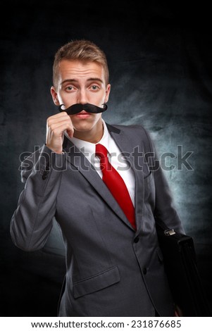 Wants to grow up as soon as possible.Young businessman with fake mustaches pretends to be older isolated on white background