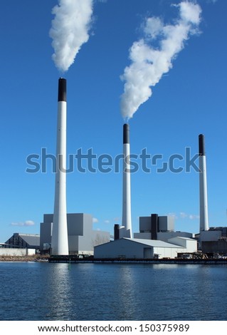 Factory chimneys at energy plant with blue sky and lake. Focus on a global green environment, and a healthy surrounding.