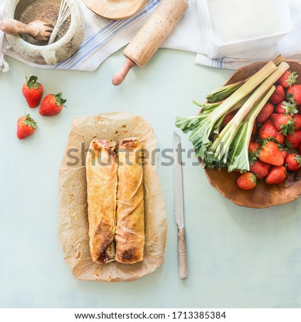 Image, Stock Photo Strawberry rhubarb strudel cake on light mint kitchen table with knife and ingredients. Top view. Homemade seasonal baking