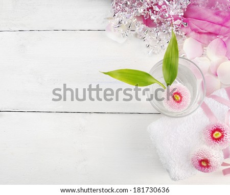 pink spa set, daisies flowers  in glass of water , rolled up towel on white wooden background
