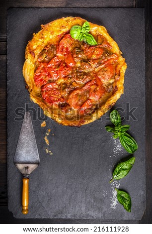 Tomato tart tatin on black slate with basil and kitchen utensils ,top view, food background