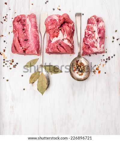 raw pork fillet with spices and bay leaf in spoon on white wooden background, with copy space, top view