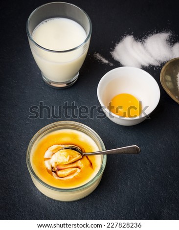 creme brulee with spoon, glass of milk, egg yolk and sugar on dark background
