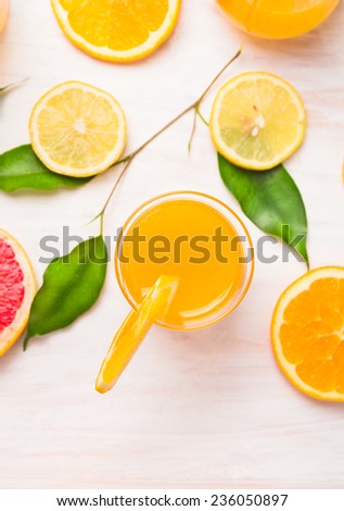 orange juice glass with  slices of citrus and green leaves on white wooden background, top view