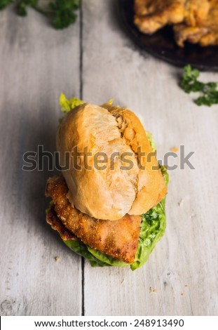 Roll with fried schnitzel  and salad leaves on old wooden background, german tradition food