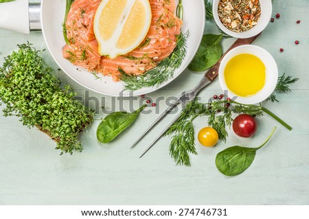 Salmon with lemon, oil and fresh seasoning in white pan on rustic wooden background, top view