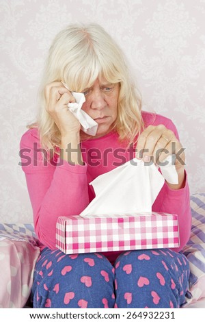Sad woman with pink pajama and tissues sitting on floor against bed