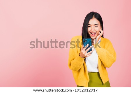 Happy Asian portrait beautiful cute young woman teen smiling excited using smart mobile phone studio shot isolated on pink background, Thai female surprised making winner gesture on smartphone