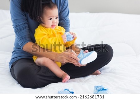 Asian young mother sitting on the bed wearing shoes to his cute baby little girl toddler on bedroom, Mom helping little infant wears shoes Photo stock © 