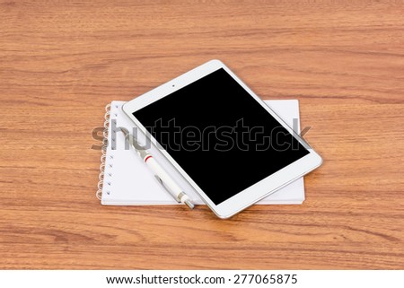 White digital Tablet on wooden table with pencil and book note