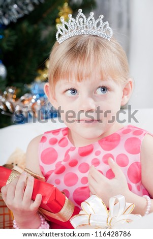 fair-haired girl in a pink dress with a New Year\'s gift at a fur-tree