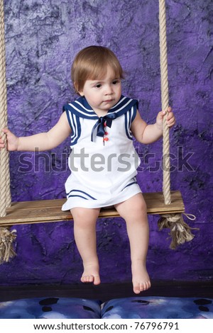 little girl in a dress in sailor\'s style sits on a rope swing. Studio shooting.