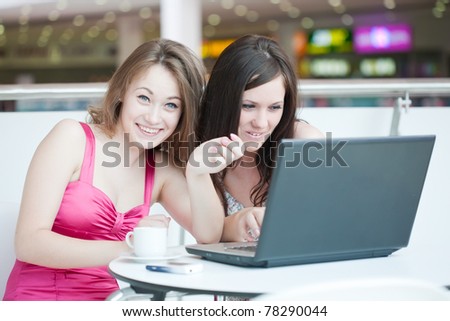 Two girls work on a laptop, sitting in cafe in shopping center