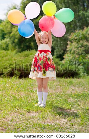 Happy girl with balloons walking on the spring field