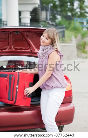 girl stacks a suitcase in a car luggage carrier