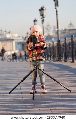 little girl with the big camera on a support  stand on the street and photographs