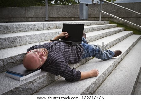 A sleeping / resting / exhausted man working with his computer / laptop in stairs outside.