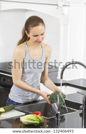 Young fit / healthy / sporty woman washing / prepare vegetables and fruit. Modern and exclusive kitchen.