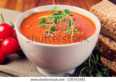 Delicious gourmet tomato soup with fresh herbs and pepper. Bread, oregano and tomatoes on the side.