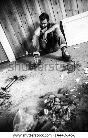 Punk rocker or redneck sits on the floor and think in messy house.
