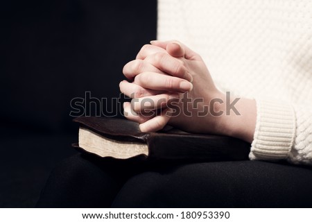 Woman folding hands over her holy bible and praying to God.