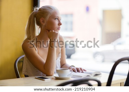 Pensive young woman at cafe looks out the window