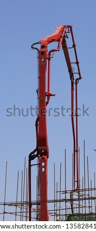Huge concrete pump with tall arm pumping concrete on top of the building with workes