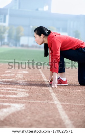 Athletic Chinese woman in start position on track