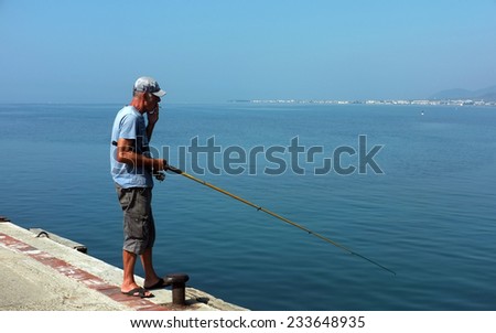 AKCAY, TURKEY- AUGUST 15, 2014:  Elderly man angles on concrete pier while smoking in Akcay, Turkey