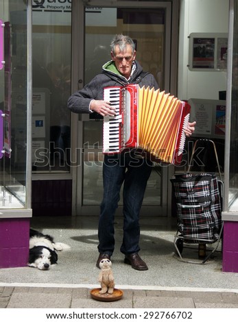 HASTINGS, UK - MAY 04, 2015: Street musician plays accordion to earn money while his dog lays beside in front of a closed shop in Hastings, UK.
