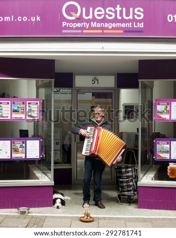 HASTINGS, UK - MAY 04, 2015: Street musician plays accordion to earn money while his dog lays beside in front of an estate agent in Hastings, UK.