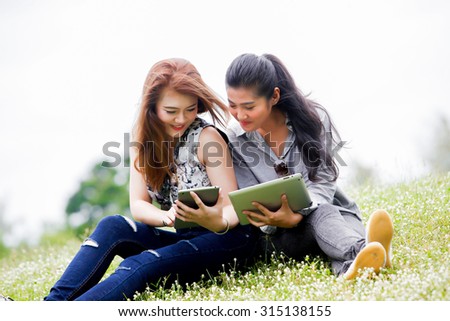 asian woman relaxing in the park and reading her tablet for business and vacation