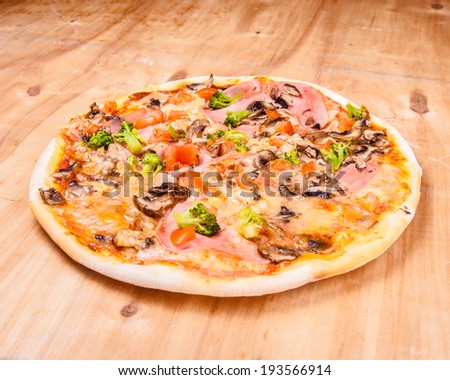 pizza with mozzarella,  ham, mushrooms chicken, broccoli, and tomatoes, whole, uncut, on wooden table