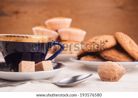 Blue china cup with brown sugar, cookies, and muffins on table