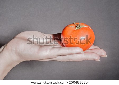 Female hand holding red tomato against black background as a metaphor for concepts of health, life, and ideas