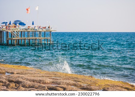 pier on the rocky sea shore, people swimming and jumping in water, turkish flag in background
