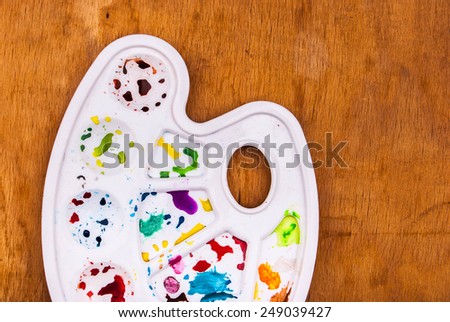 White plastic art palette with random watercolor paint blobs on wood