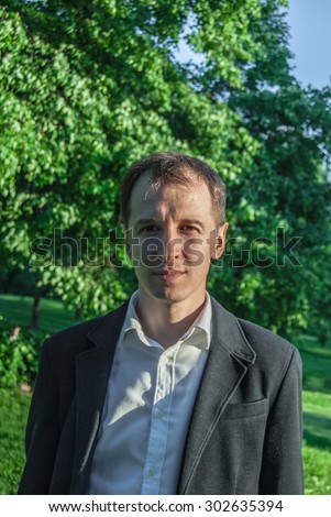 Young man in formal outfit looking seriously in camera, outdoors on the green background. Business man in a green zone or park. An image for topics of finance and business.