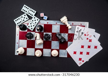 Various board games and figurines over checkers board and dark background. Metaphor for gaming and gambling.