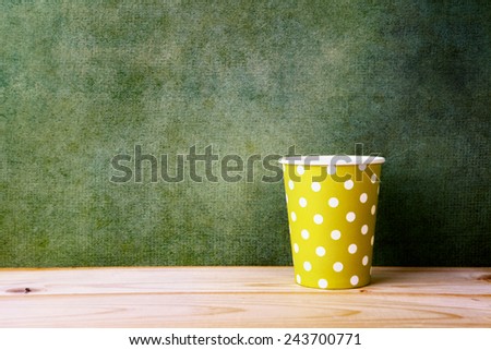 yellow polka dot paper glass on wooden table over retro green background