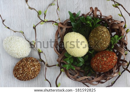 Easter decorations / cards hand-decorated Easter eggs an unusually covered in rice, buckwheat, spices and couscous with boxwood in rattan nest on  wooden background / on the table with willow sticks