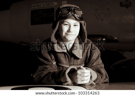 Smiling young pilot with goggles resting on airplane wing, smiling at the camera