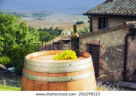 Red wine bottle and glass on wooden barrel in the background of the Tuscan landscape, Italy