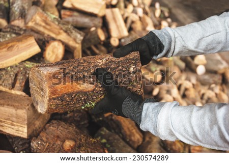 Firewood in a piece of wood stored on the stack, hands holding a piece of firewood