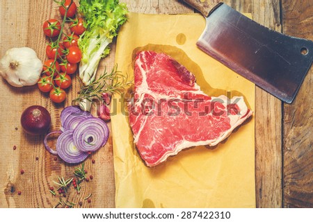 Meat with fresh vegetables, spices and meat cleaver on a wooden table vintage