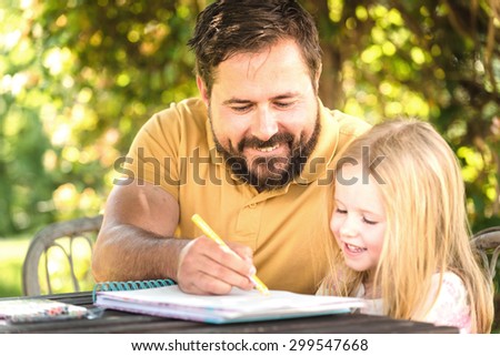 Father with daughter in the garden at the table, doing homework in a summer day.
