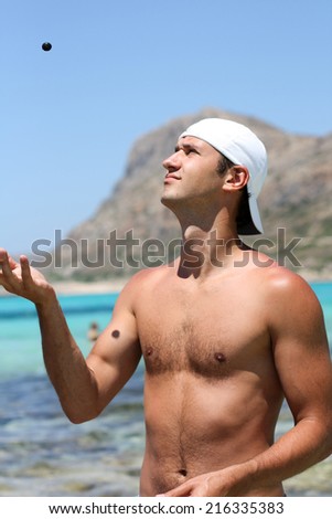 Young man is standing on the beach and throwing a little stone
